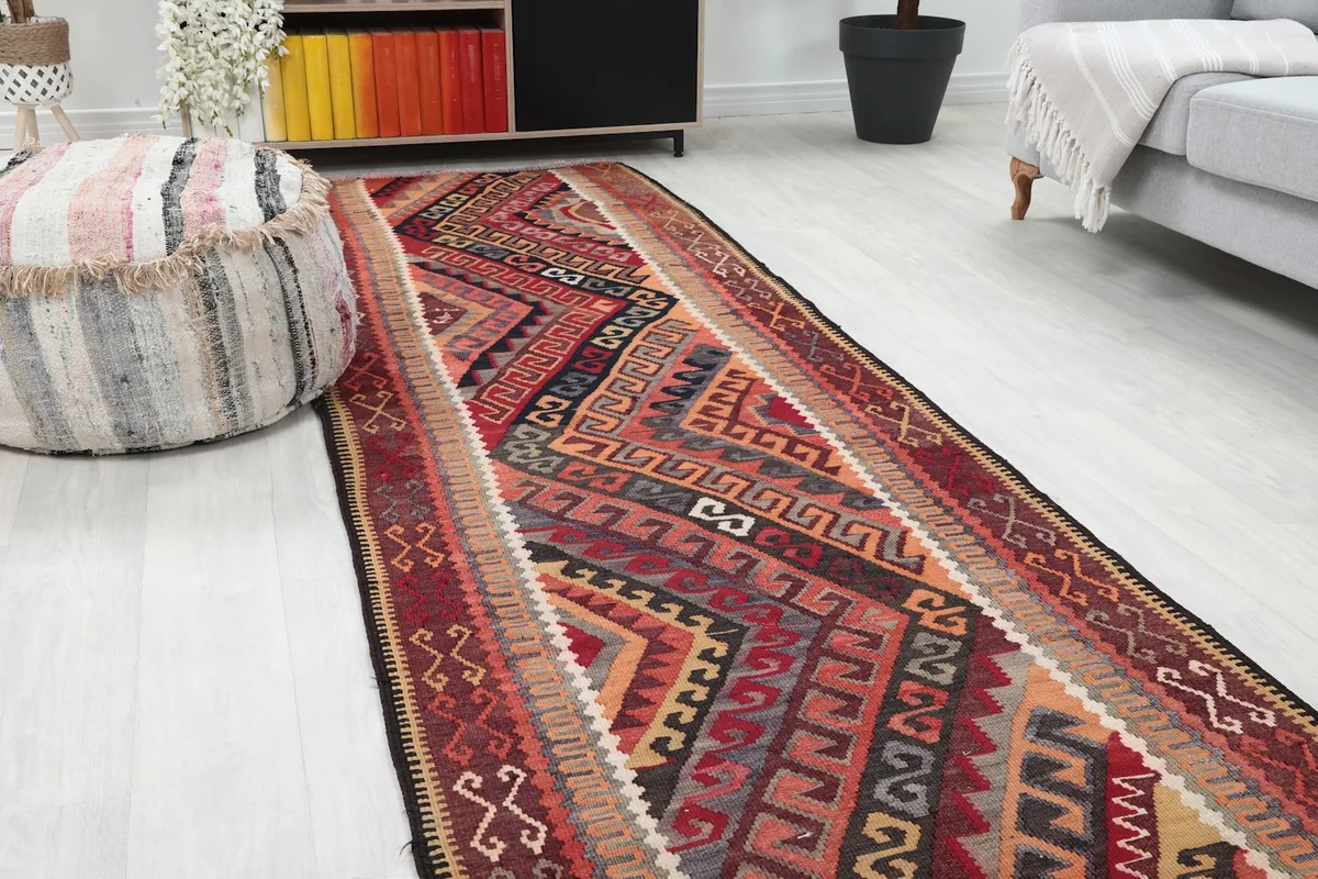 Close-up angle view of the runner rug's red and black geometric patterns next to a decorative ottoman.