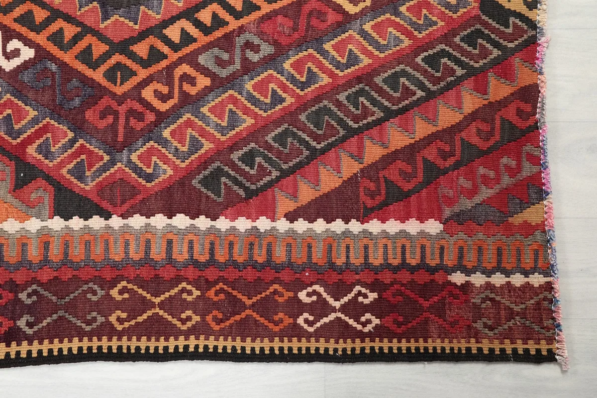 Detailed view of the intricate border and central geometric motifs in red, rust, and beige.