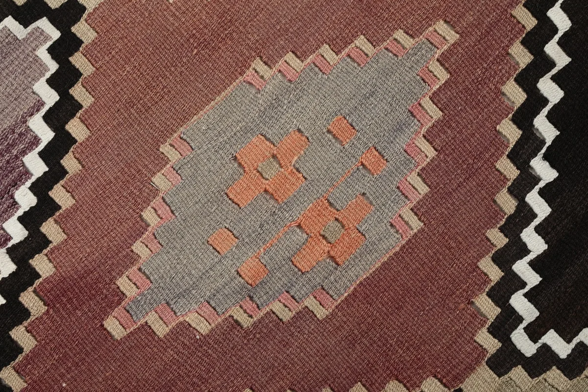 Close-up of a single rose and gray diamond motif with orange accents within the rug's pattern
