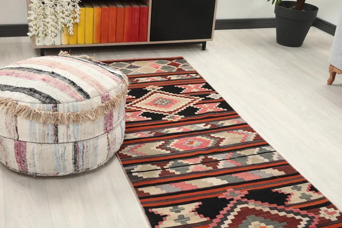 Close-up view of the runner rug on the floor next to a round striped ottoman and console table