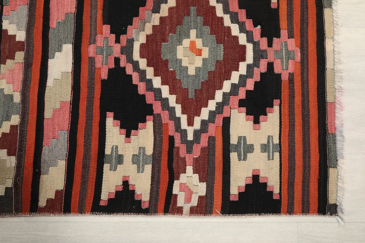 Detailed view of the rug's hand-knotted texture and geometric patterns in black, pink, and beige