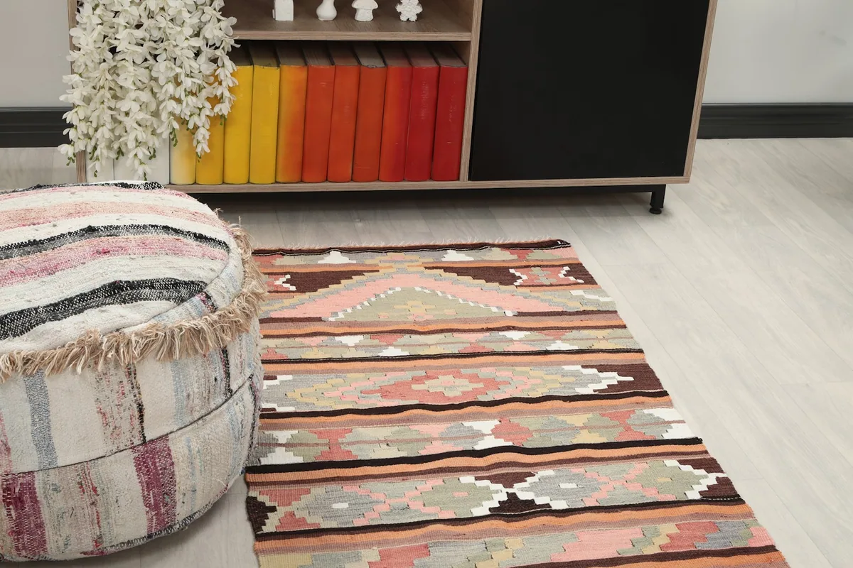 Close-up angled view of the rug's geometric patterns and colors next to a striped pouf