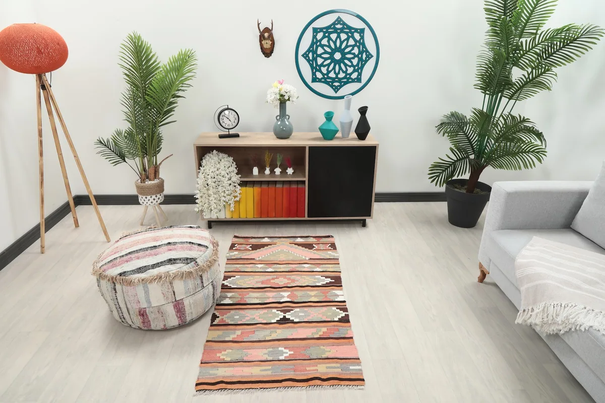 Vintage pink and orange rug placed in a living room setting with a light gray sofa and wooden cabinet