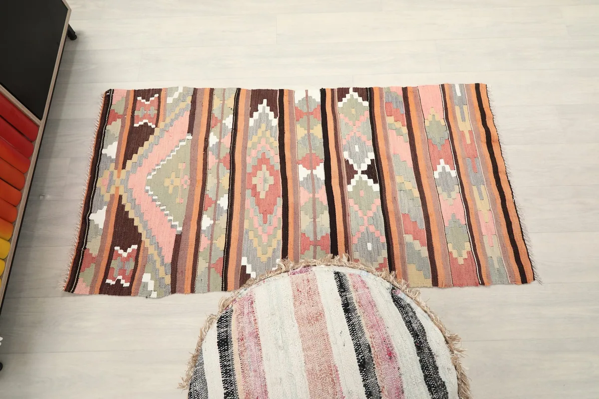 Full overhead view of the rug on a light floor, with a decorative pouf in the foreground