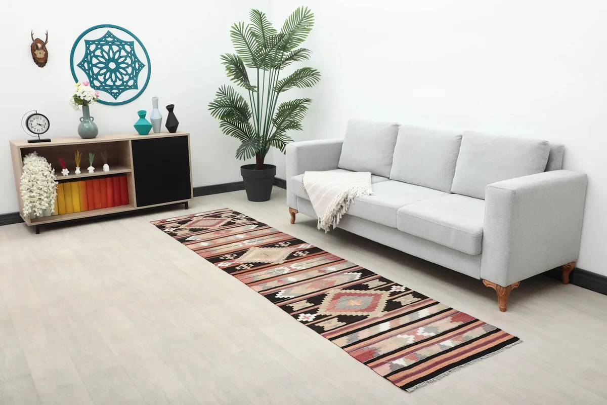 Long view of the black and rose runner in a room with a sofa, plant, and decorative shelf