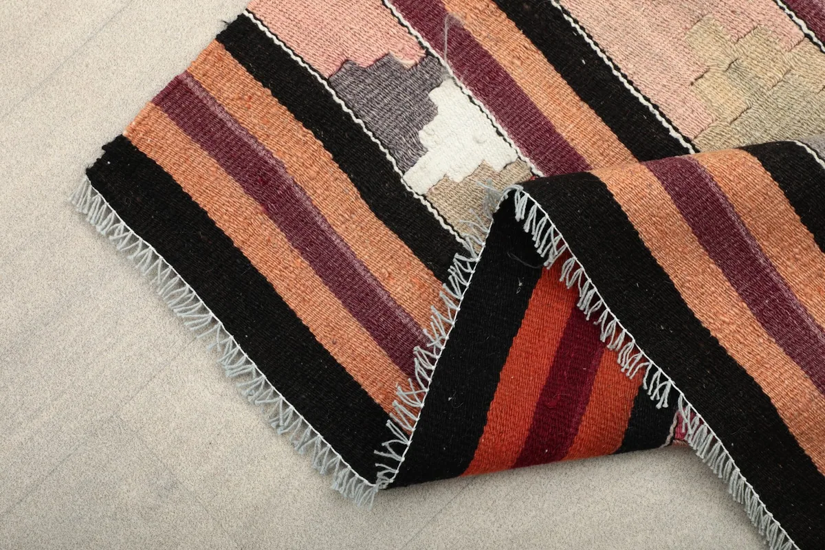 Folded edge of the runner, displaying the striped patterns in black, orange, and rose