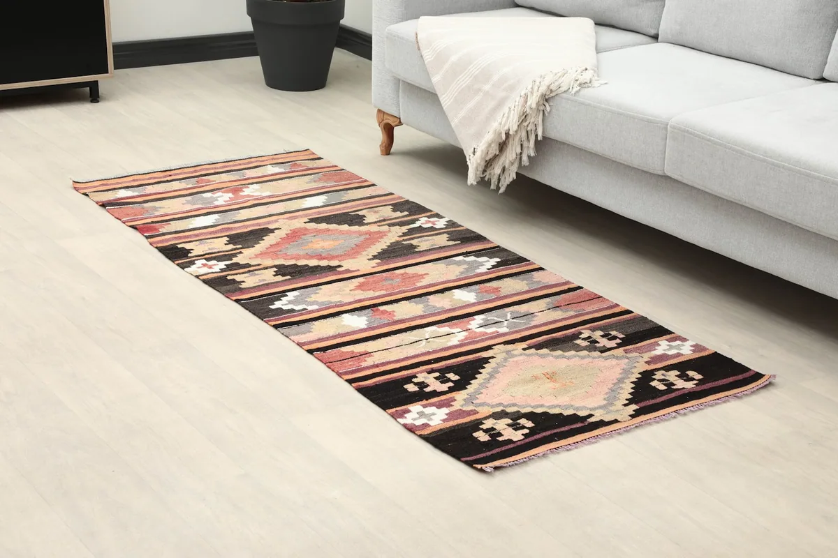 Angled view of the rug in a room, highlighting its black, rose, and tan colors