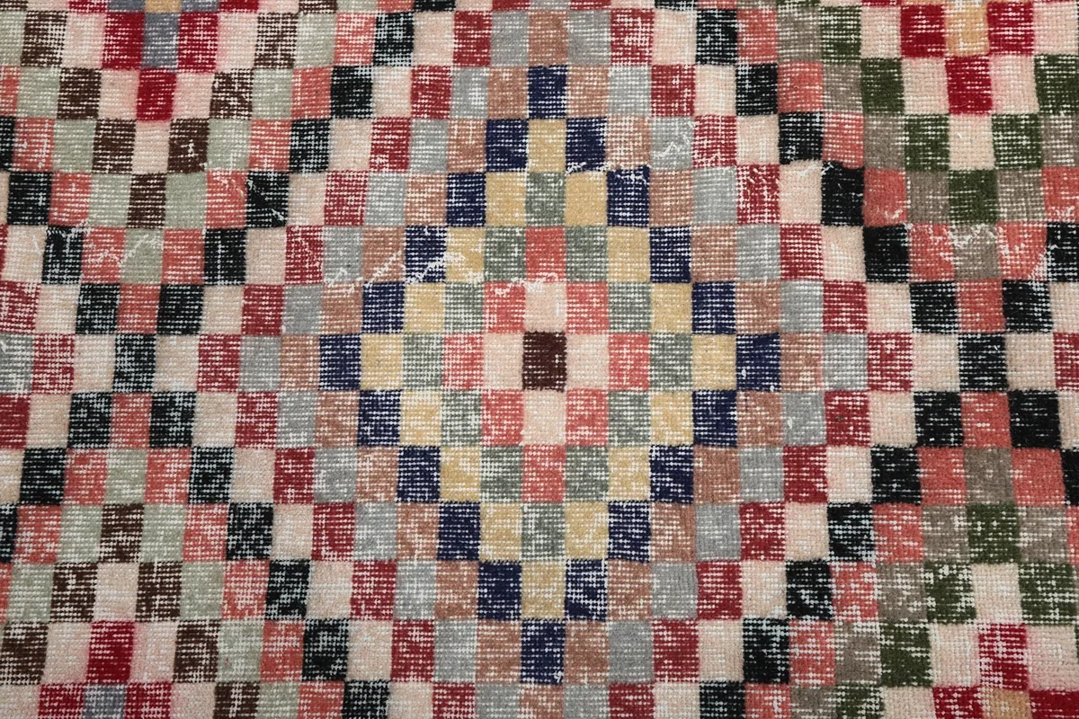 Close-up detail of the individual colored squares forming the geometric motif on the vintage rug.