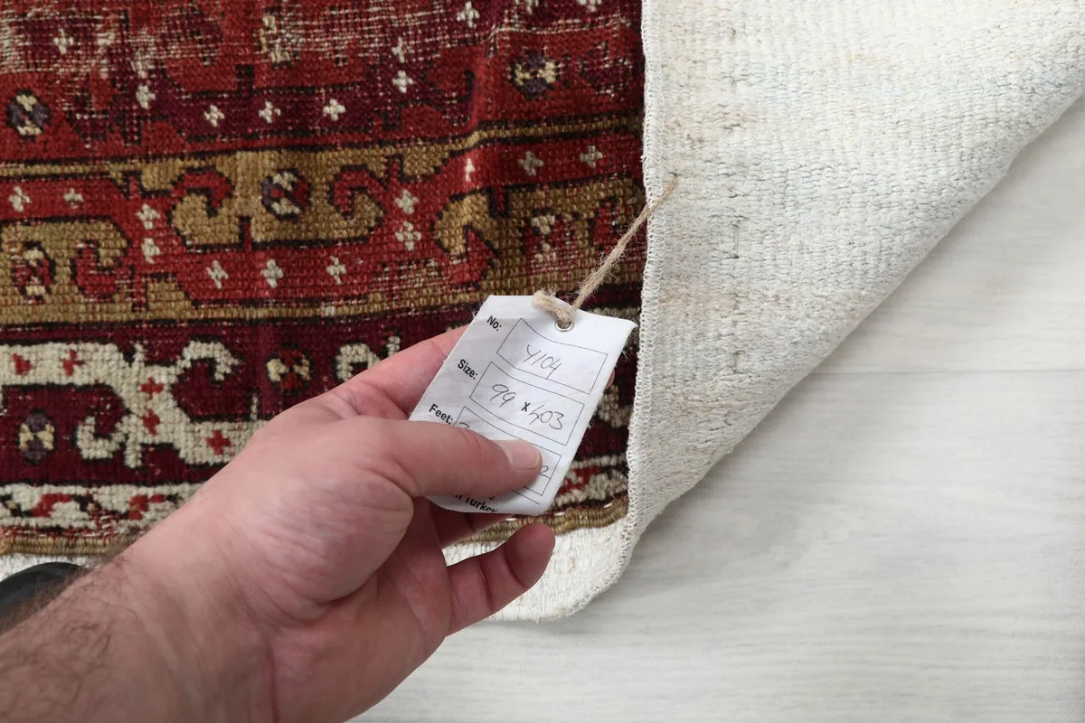 Hand holding the product tag, displaying the rug's dimensions of 99 x 403 cm.