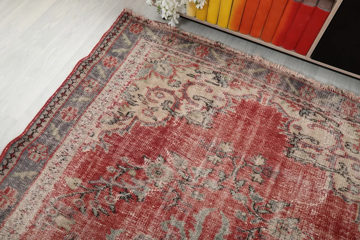 Corner view of the vintage rug, showing the faded red field and the patterned border