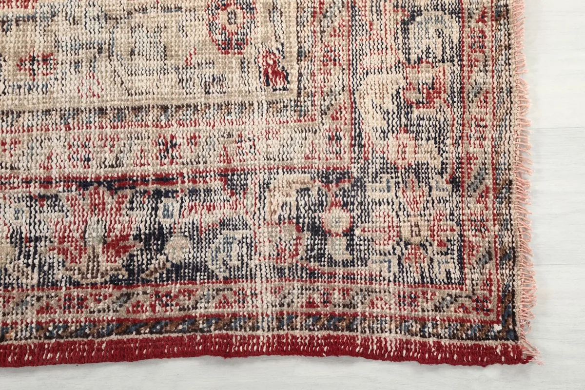 Detail of the rug's border showing faded red, beige, and navy patterns