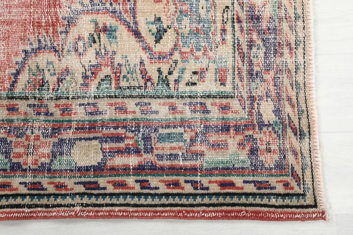 Detail of the rug's border, featuring geometric patterns in blue, beige, and rose tones.