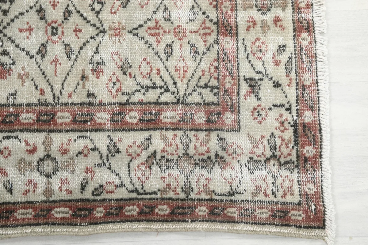 Detailed view of the rug's corner, showing the cream field, rose and olive motifs, and rust border