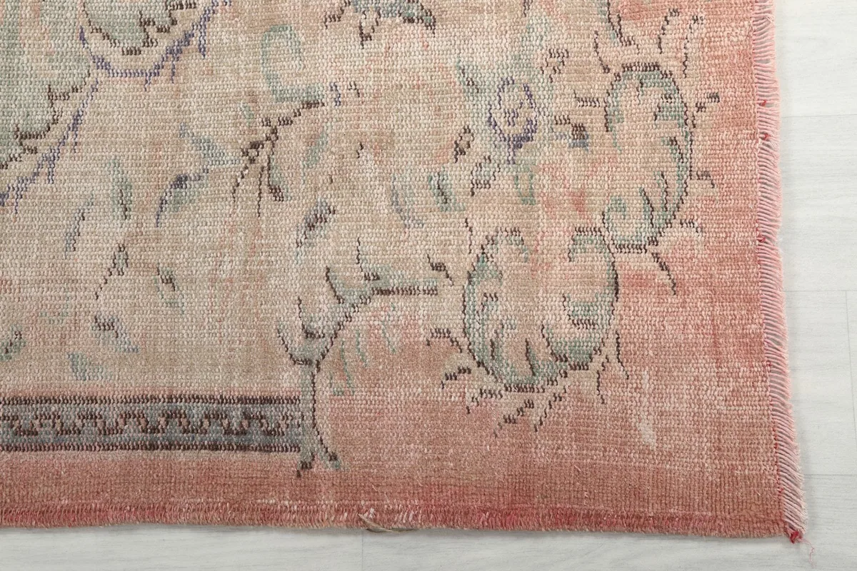 Detail of the rug's outer border and corner, showing the faded rose color and fringe