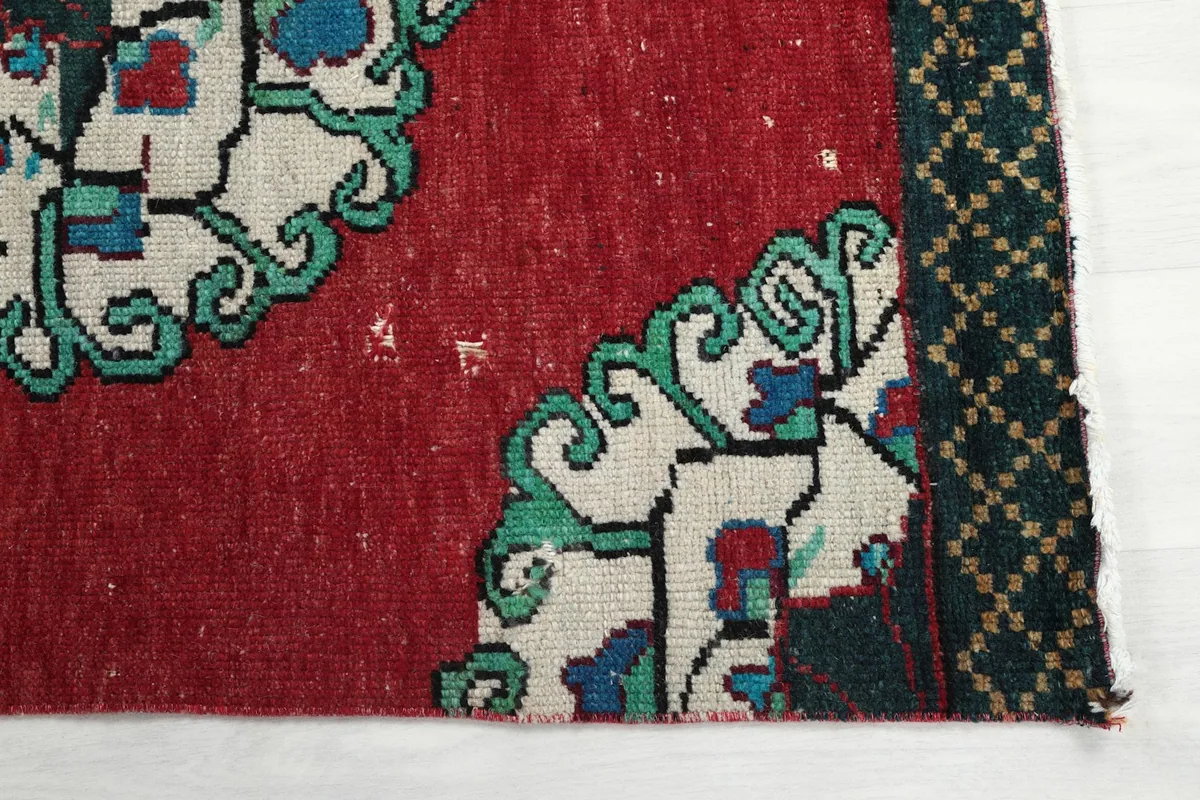 Detailed view of the rug's red field, a medallion edge, and the green border, showing patina.
