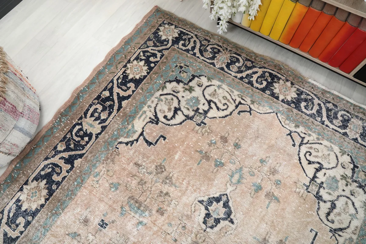 Angled view showcasing the beige field and the detailed navy and gray outer border of the rug