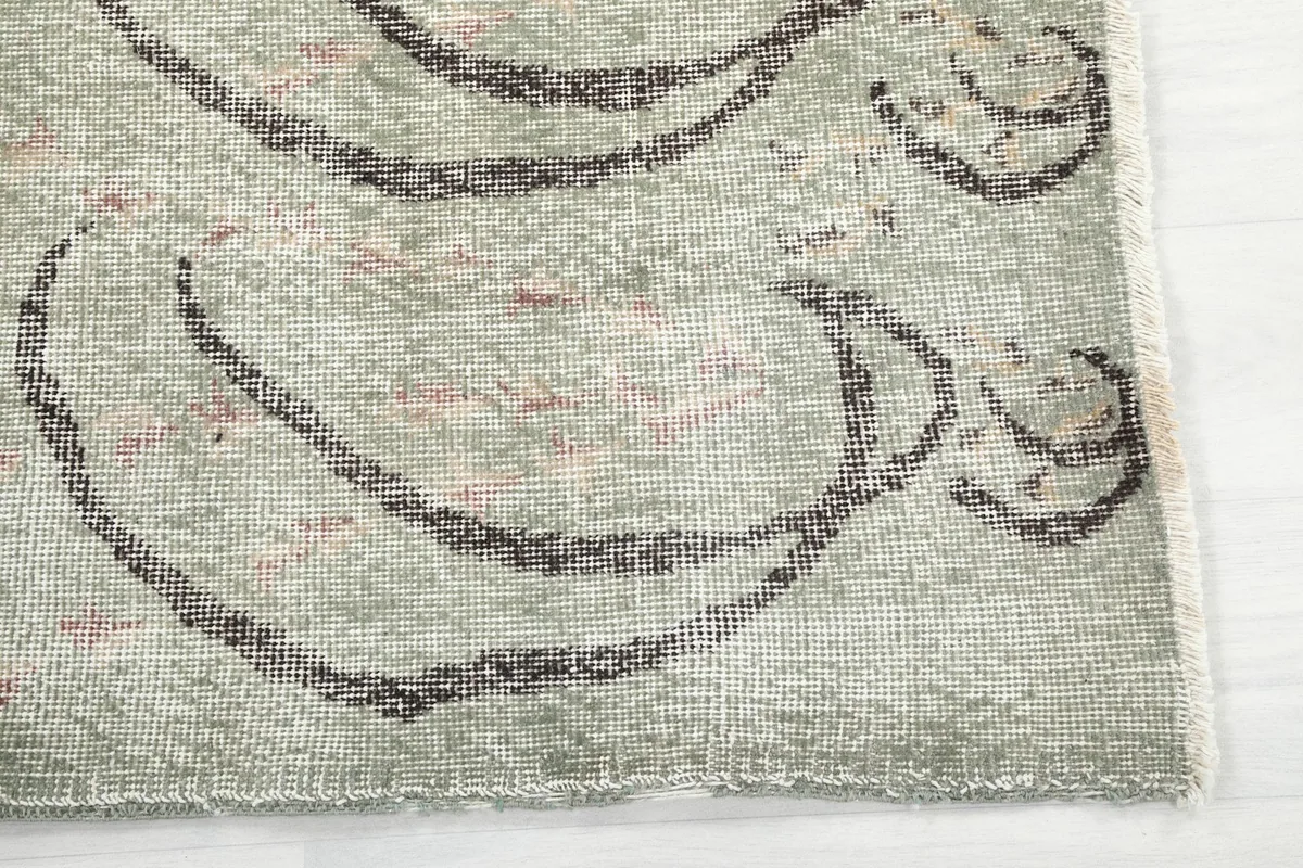 Detailed view of the rug's edge, showing the hand-knotted wool pile, green field, and charcoal design.