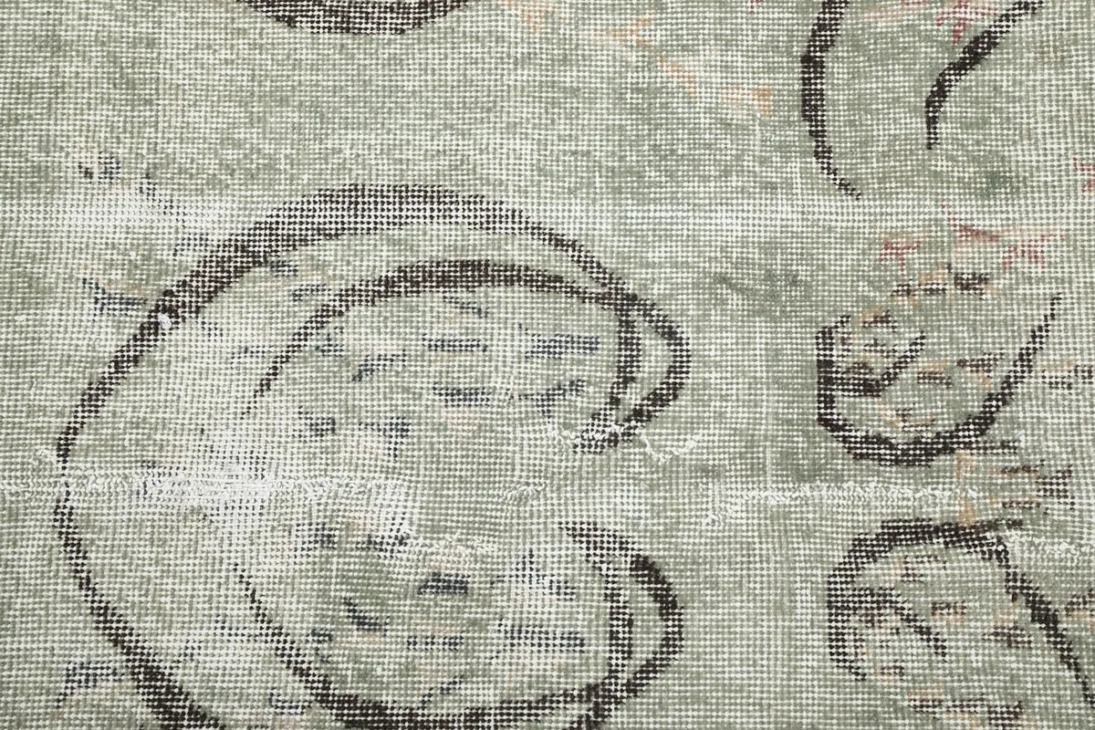 Close-up of the low wool pile and hand-knotted texture, revealing the green and charcoal colors with subtle rose fading.