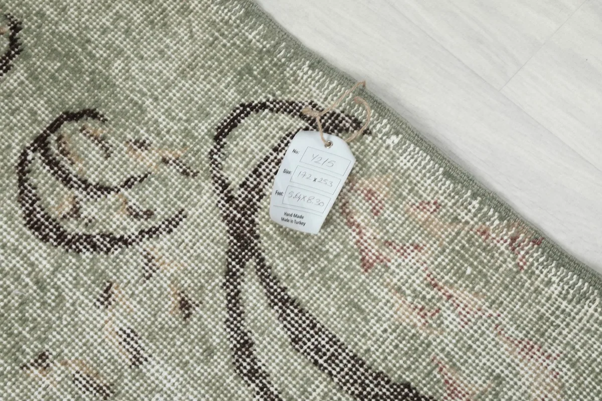 Detail of the rug's surface with a product tag, highlighting the texture and faded colors of the vintage wool.