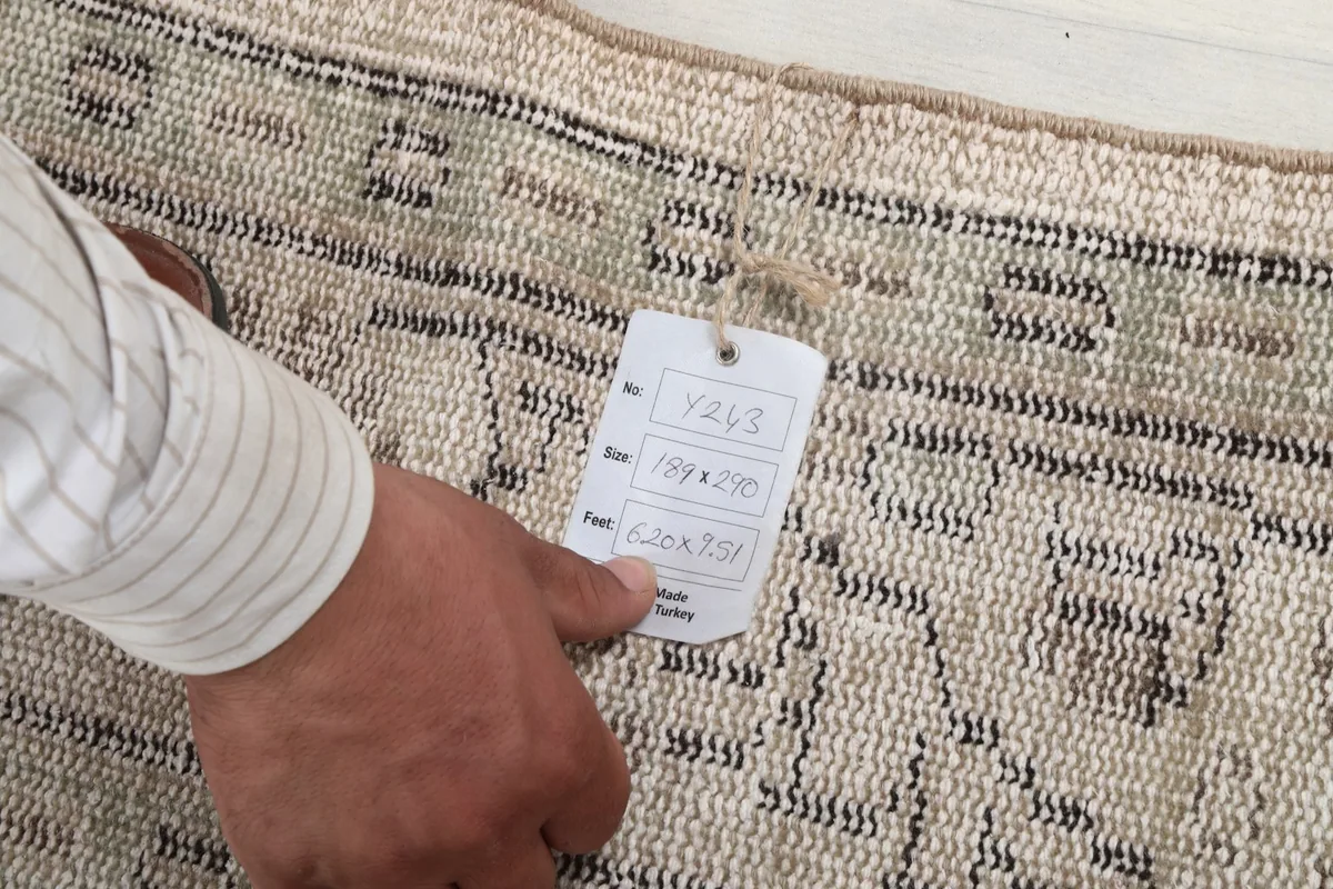 Hand holding a tag showing the rug's dimensions in centimeters and feet