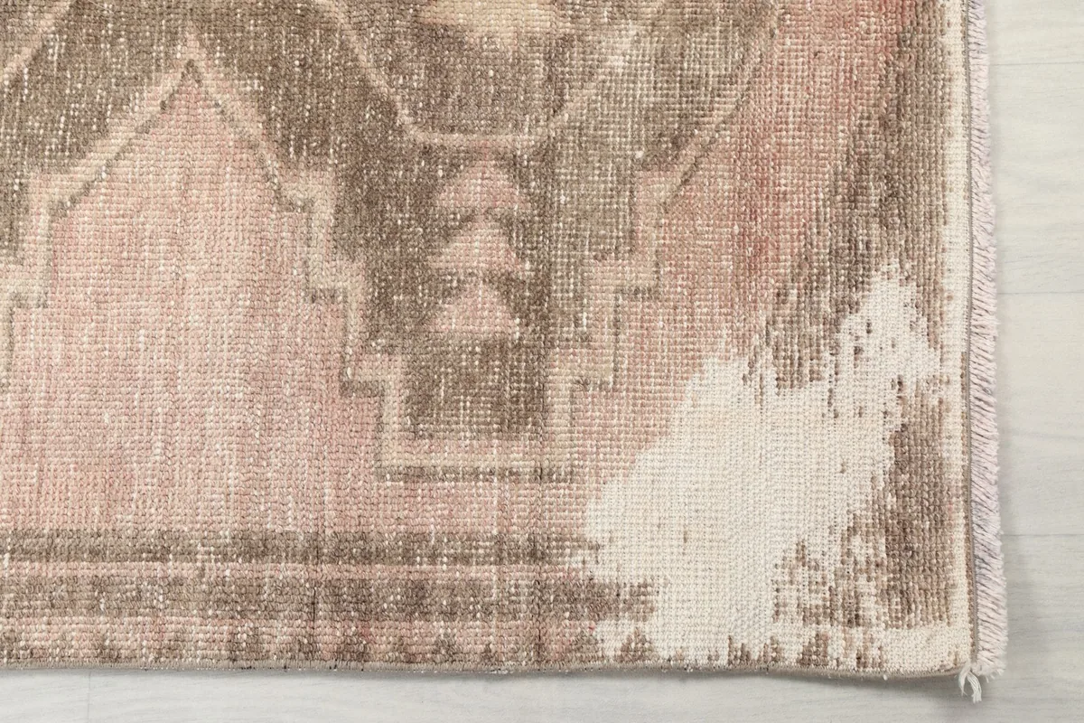 Detailed view of the rug's end, showing the rose and gray geometric patterns and areas of wear.