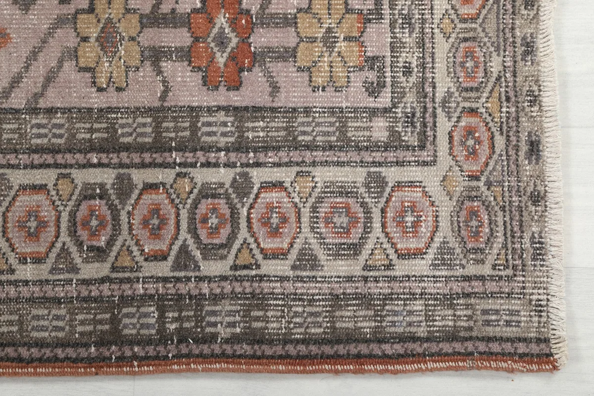Detail of the rug's border pattern, featuring geometric shapes in gray, beige, and rust tones.