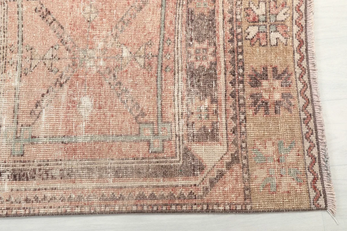Detailed view of the rug's geometric motifs and border, showing areas of wear and color variation.