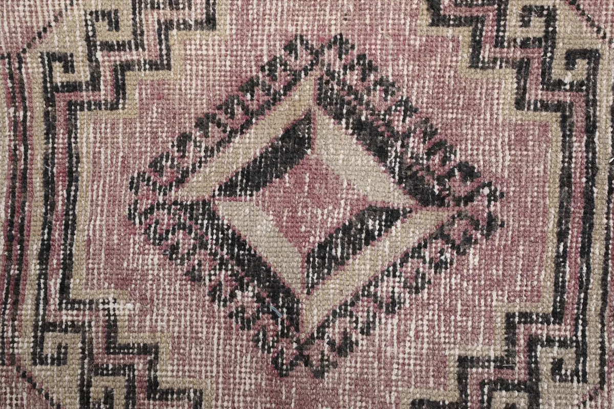 Close-up detail of a central diamond motif, revealing the black, tan, and rose color variations and low pile.