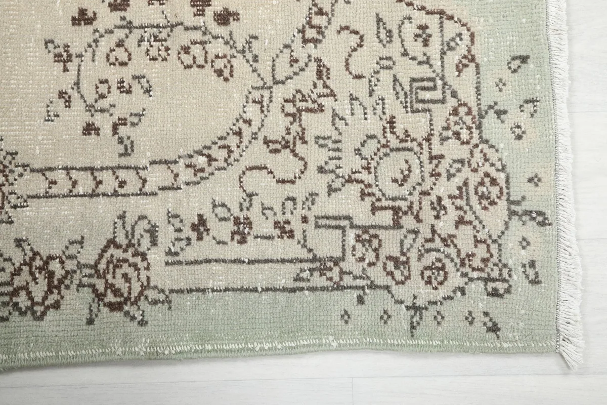 Detail of the rug's corner, showing the green border and faded brown patterns