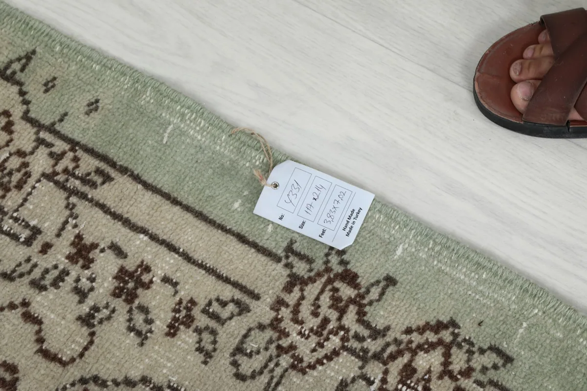 Detail of the rug's edge with a product tag, showing the muted green hue