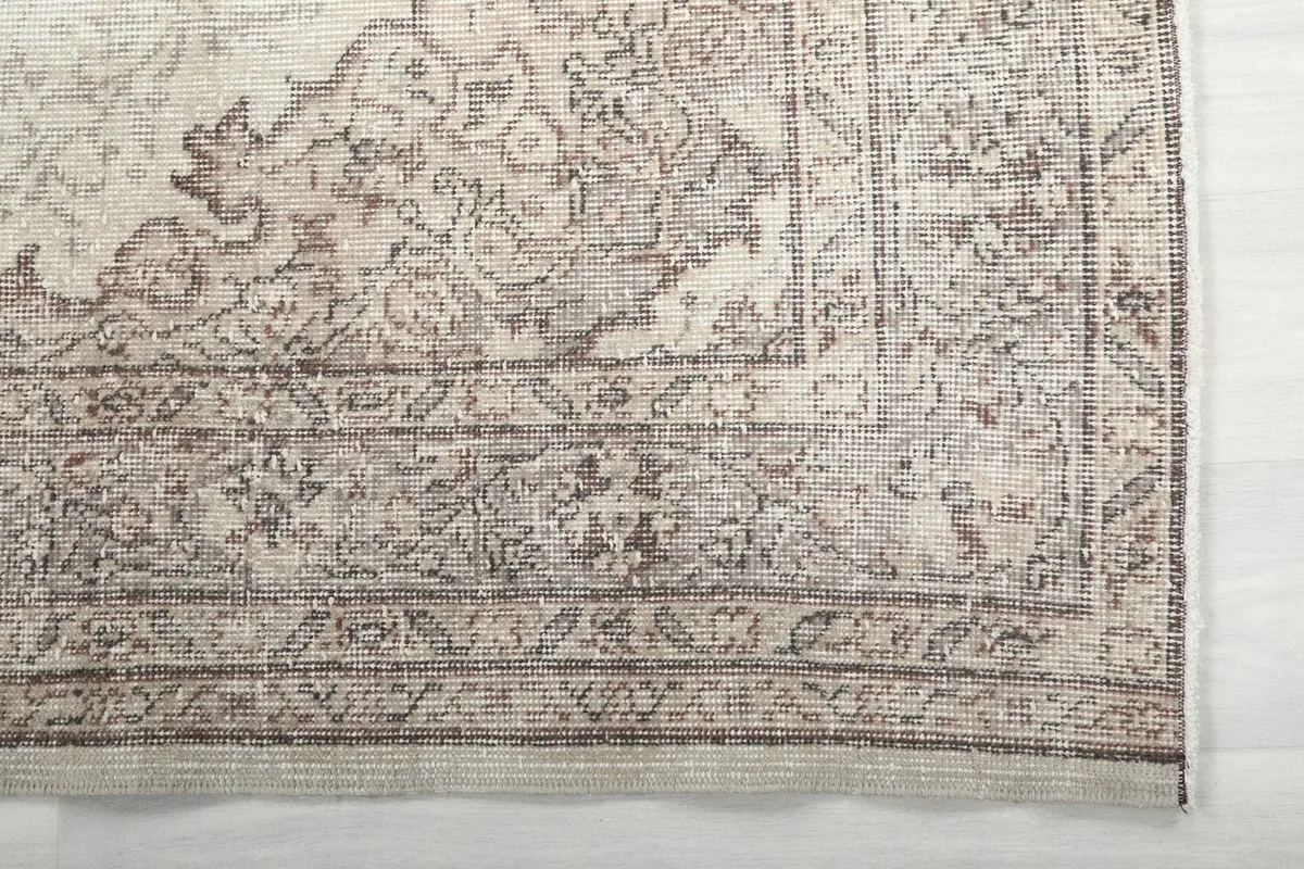 Detailed close-up of the rug's border design in brown and gray tones, showing the faded texture.