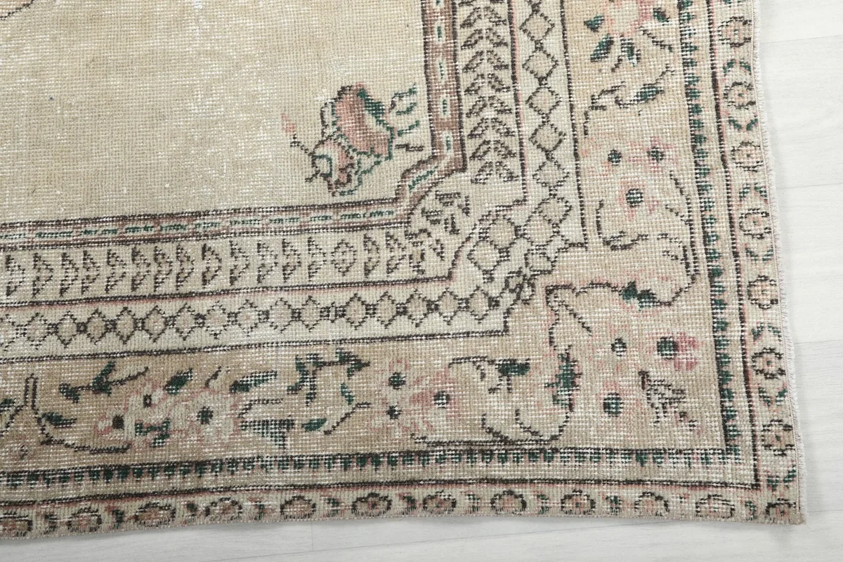 Detail of the rug's intricate border design with muted rose and green accents