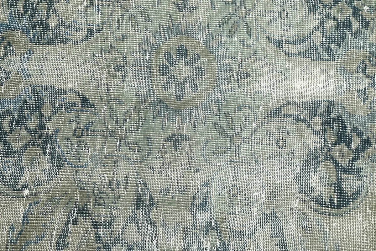 Texture and low pile of the hand-knotted wool rug showing wear and color variation