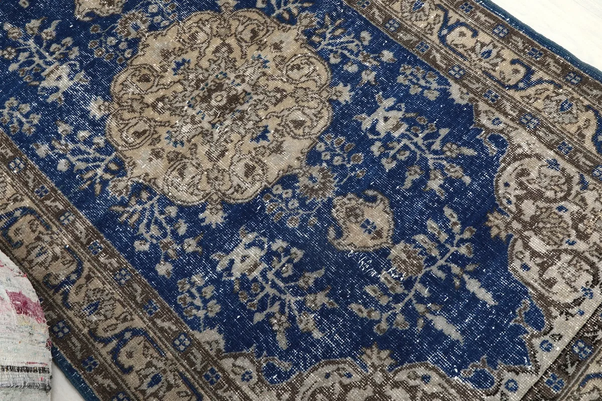 Close-up of the blue field and beige floral motifs, highlighting the aged patina of the rug