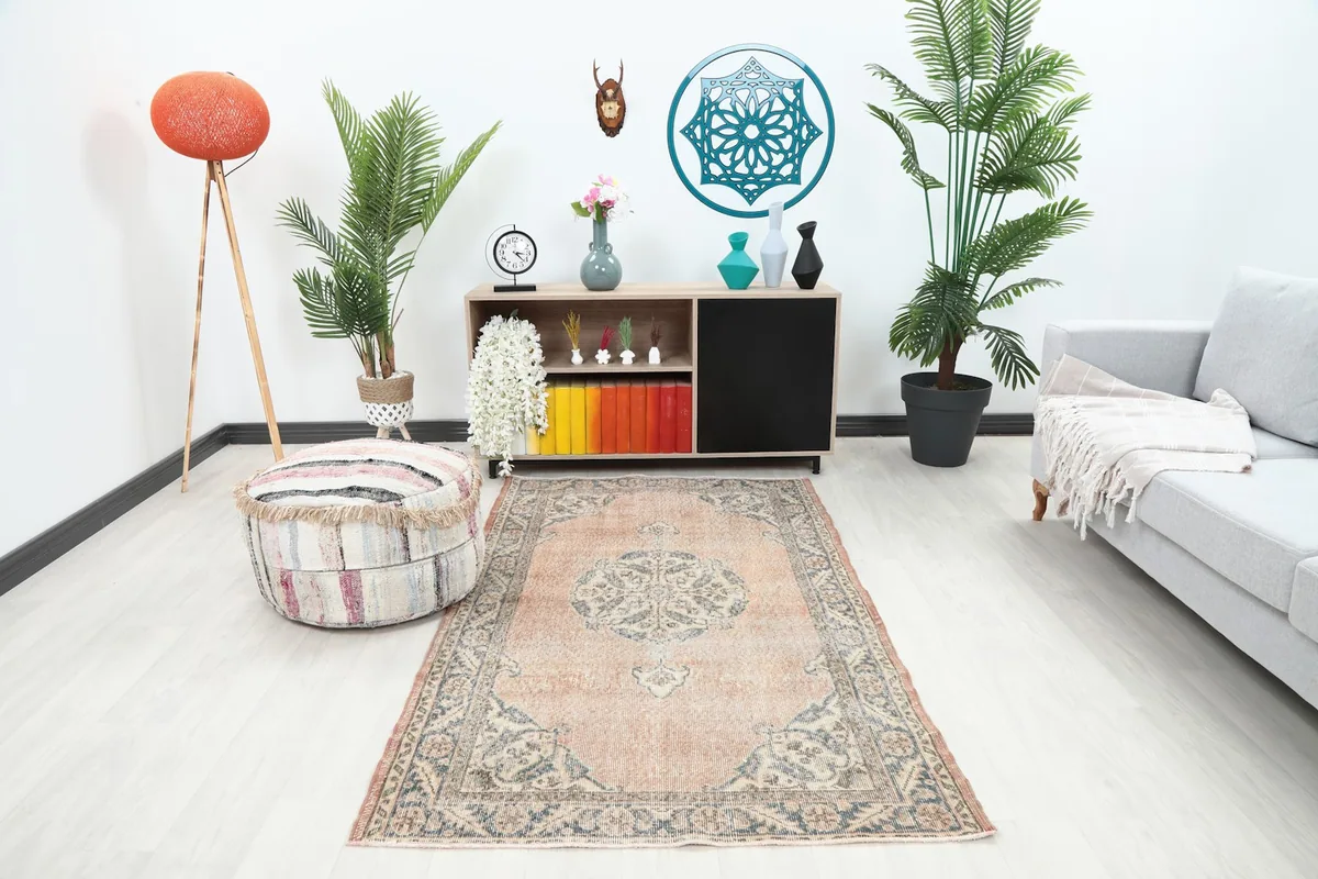 Vintage rose and blue rug displayed in a bright modern living room setting with plants and furniture.
