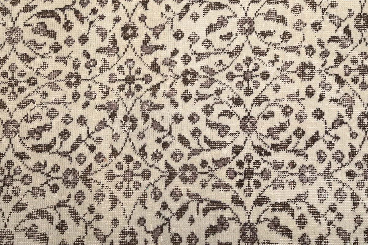 Detailed view of the intricate floral motifs in brown and tan on the ivory field of the hand-knotted rug.