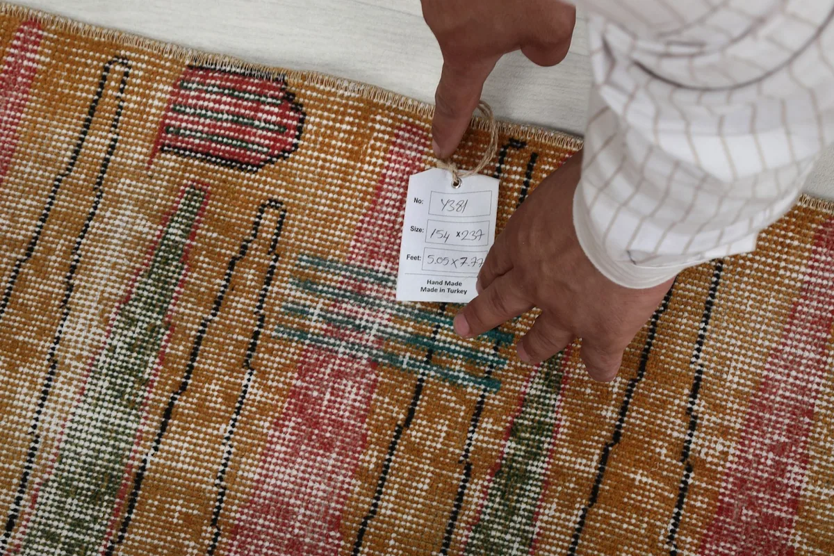 Hand holding a tag with the rug's size and origin details, showing the rug's texture