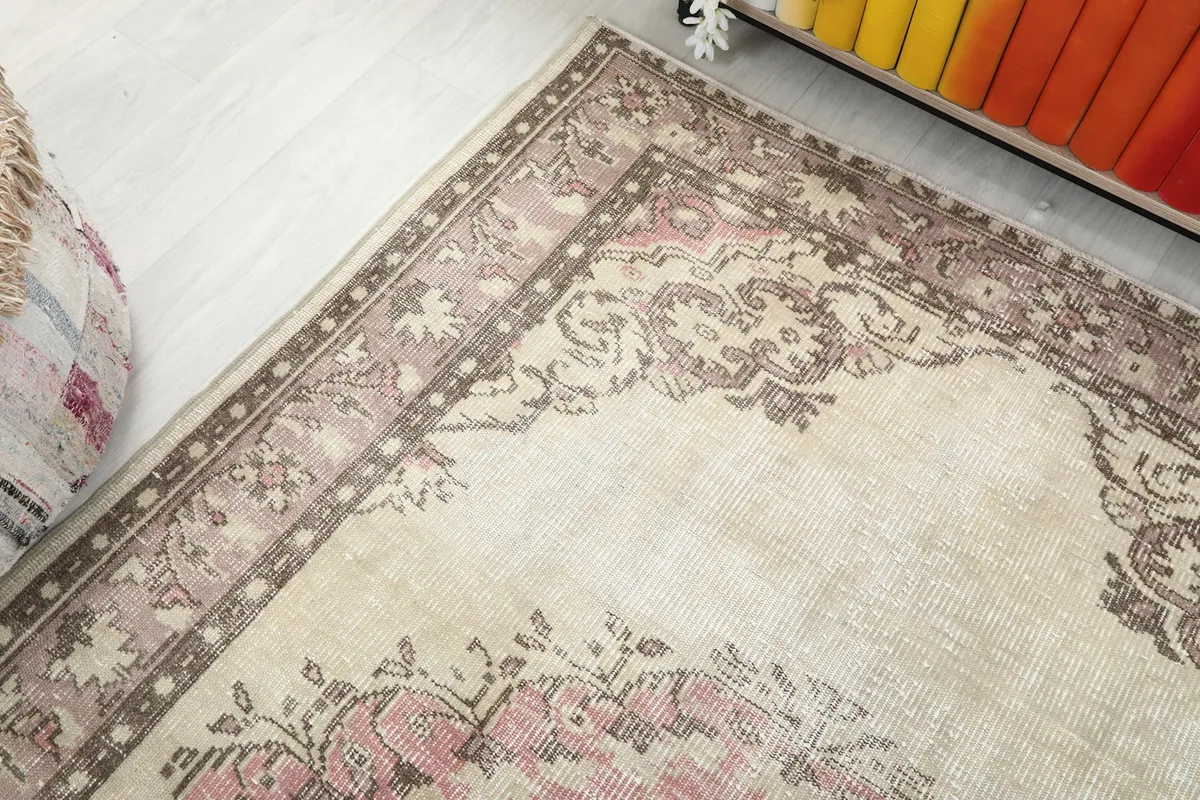 Corner view of the rug, showing the blend of cream, rose, and brown tones in the border.