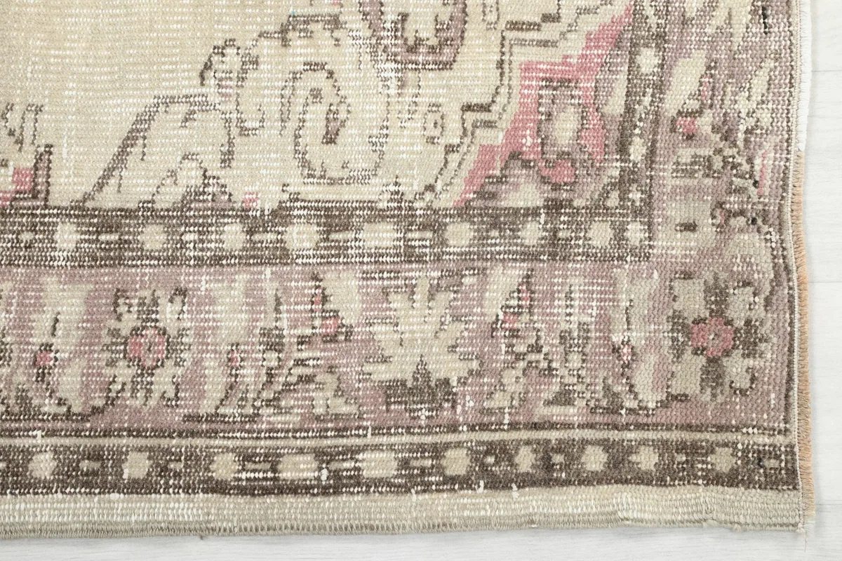 Detail of the rug's border, featuring faded brown and rose geometric patterns.