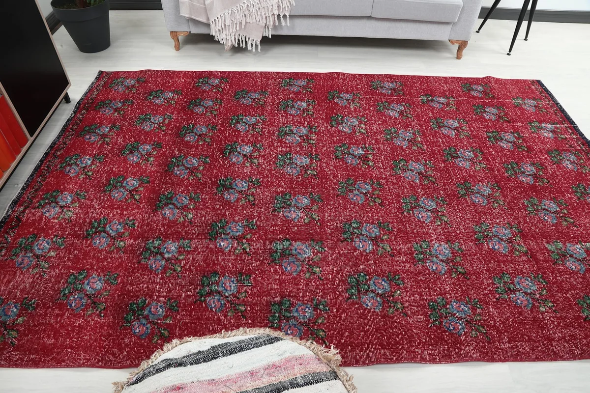 Top-down view of the red floral rug in a room, with a decorative pouf in the foreground.