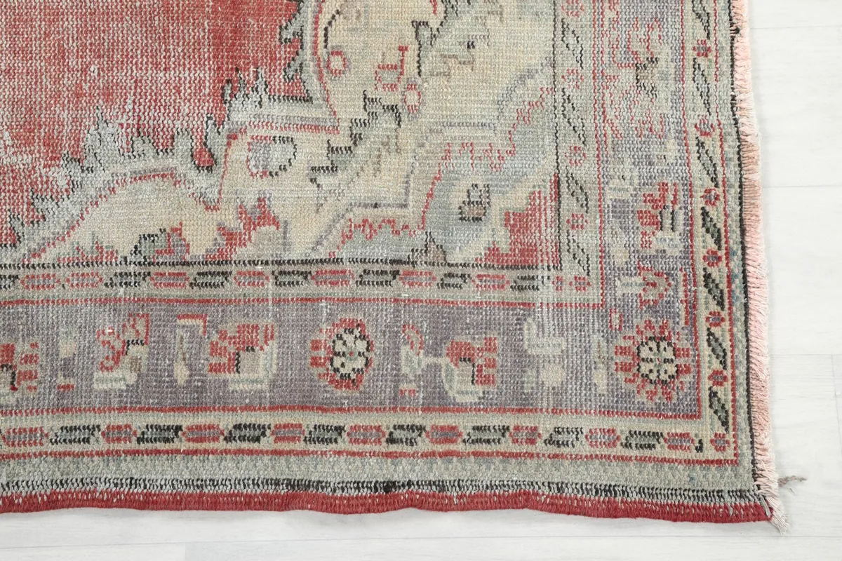 Detailed view of the intricate gray and rose border design on the vintage rug.