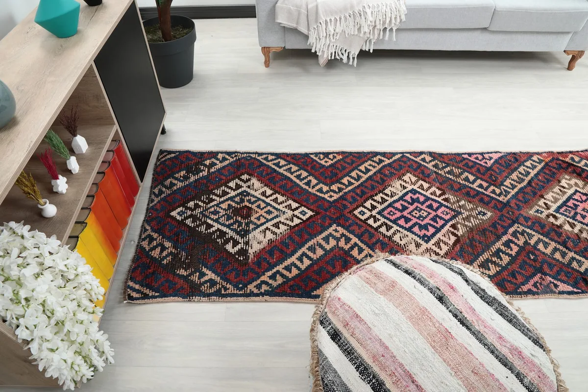 Long shot of the runner rug in the room, stretching out from a decorative pouf towards the far end.