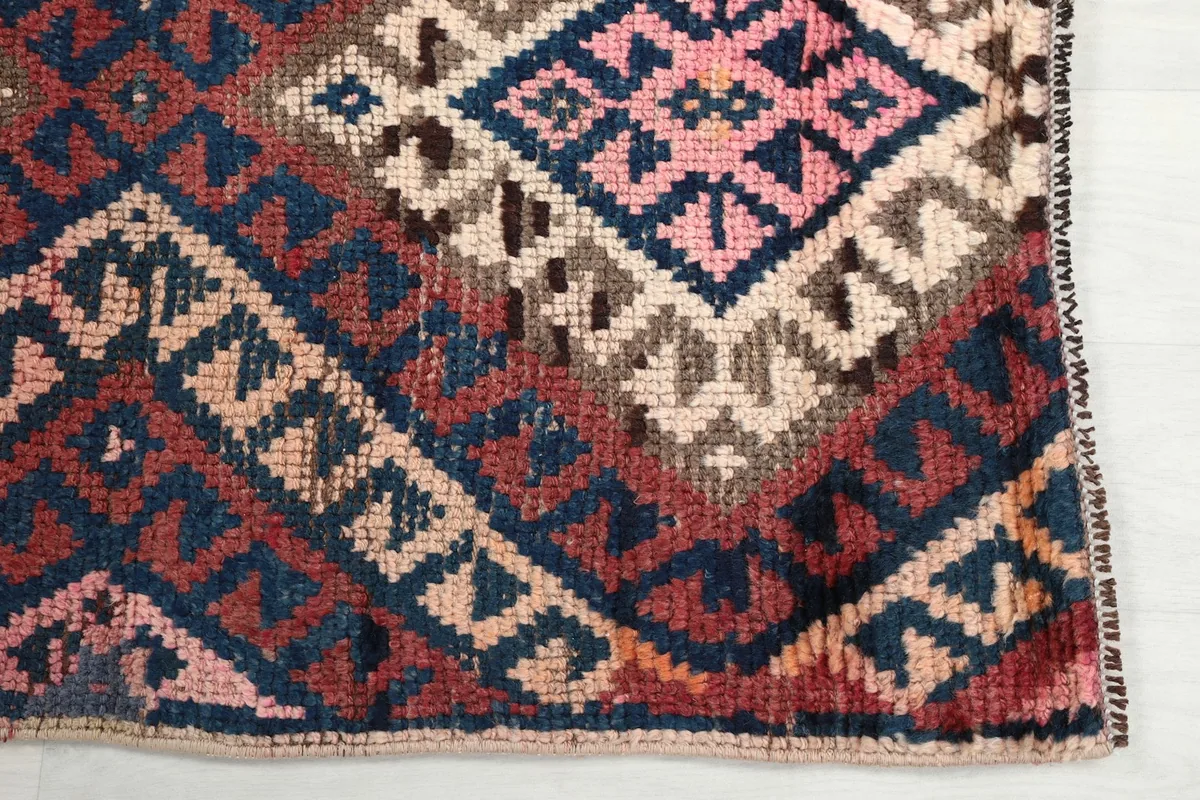 Detailed view of the hand-knotted wool pile, showcasing the navy, rust, pink, and beige colors of the pattern.