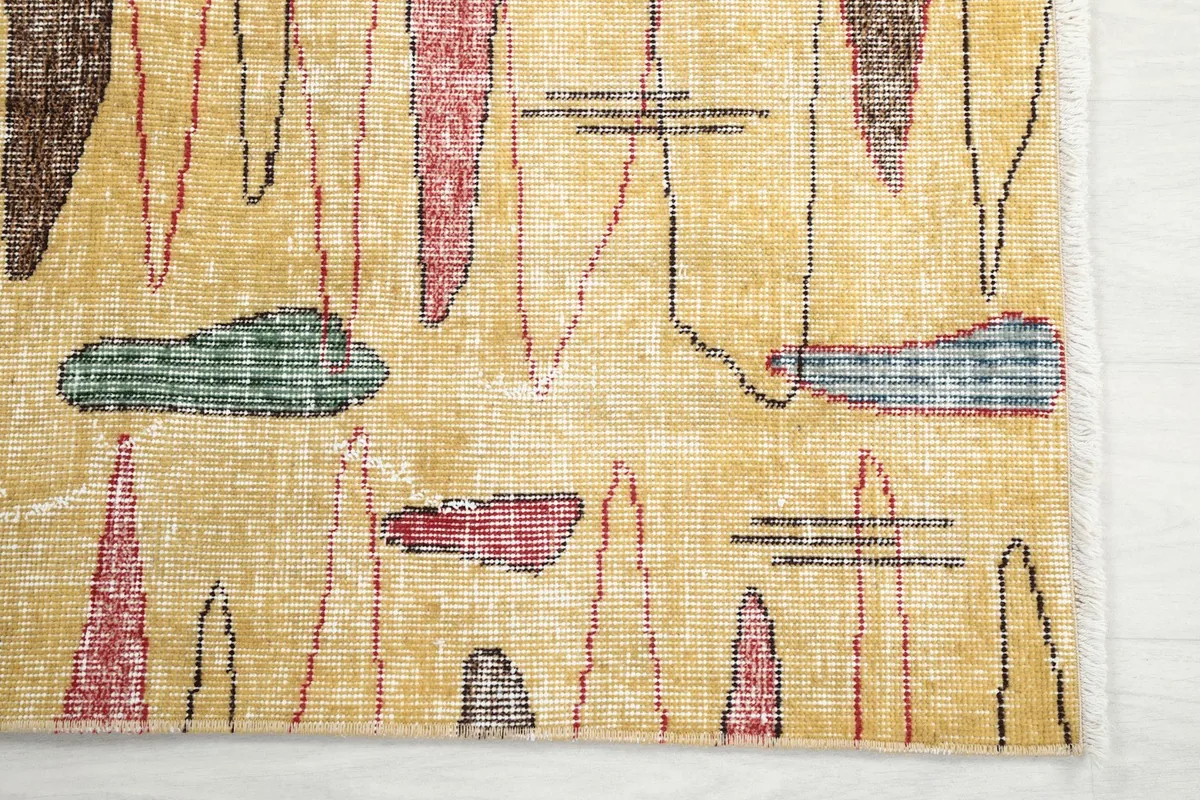 Detailed view of the rug's abstract pink, red, green, and brown shapes on a gold background
