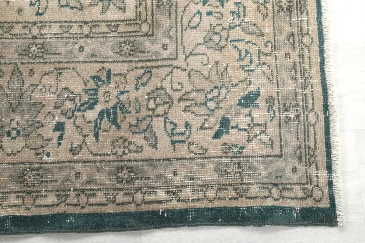 Corner detail of the rug showing the beige border with floral motifs and blue accents