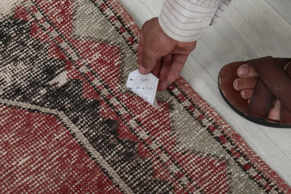 Hand holding a tag near the rug's edge, showing the texture and knotting.