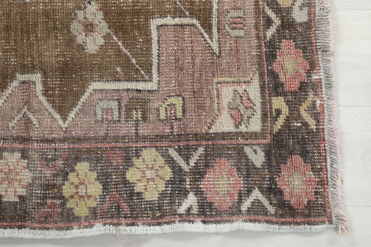 Detail of the rug's border design with geometric and floral motifs in brown, rose, and yellow tones.