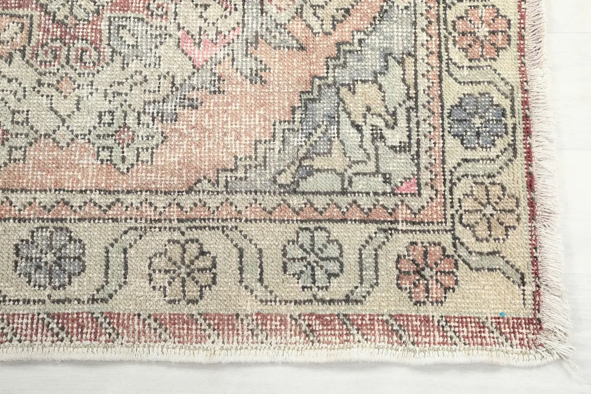 Detailed close-up of the rug's corner, showing the beige border with floral motifs and geometric patterns.
