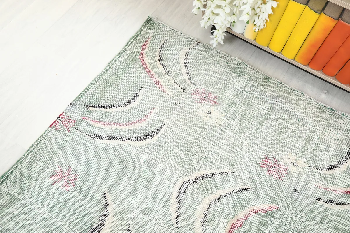 Top-down angle shot of the green vintage rug, capturing its shape and the distribution of the abstract motifs.