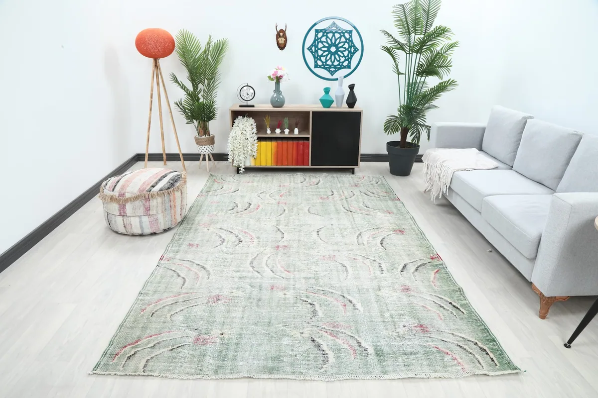 Vintage Anatolian rug with faded green and abstract rose and black motifs placed in a modern living room setting.